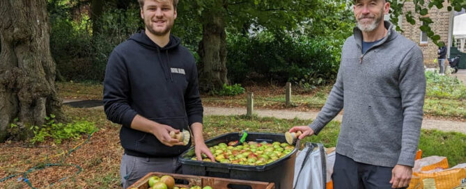 Two people standing next to box of apples